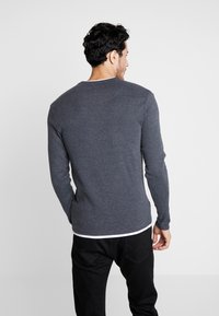 Langärmliges, dunkelgraues Shirt aus weichem Material, mit Rundhalsausschnitt und schmaler Passform, getragen mit schwarzen Hosen.
