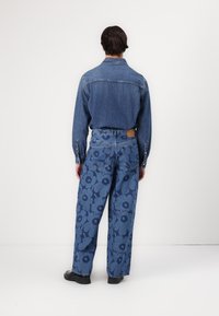 Denim ing, gallérral és hosszú ujjal, kék virágmintás bő szárú farmernadrággal párosítva, amelyhez bőr hátsó folt tartozik.