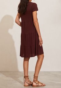 Robe courte à manches courtes de couleur bordeaux avec un design à volants, en tissu texturé, et une longueur au genou. Assortie à des sandales à brides marron.