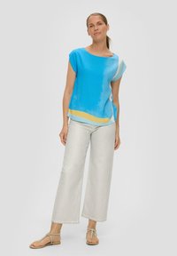 Blaues kurzärmeliges Oberteil mit gelben und weißen Akzenten, kombiniert mit hellen lässigen Hosen. Der Stoff wirkt weich mit einer glatten Textur.