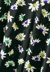 Schwarzer Stoff mit floralem Muster, das weiße Gänseblümchen, grüne und lila Akzente zeigt. Glatte Textur mit lebendigen Farben.
