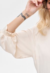 Kremowa, lekka bluzka z bufiastymi rękawami i marszczonymi mankietami. Gładka faktura z akcentem na nadgarstku.