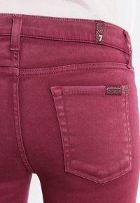 Bordeaux skinny farkut sileällä pinnalla, joissa on takatasku ja logo-etiketti vyötäröllä brändäystä varten.