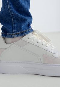 Baskets blanches avec un dessus en cuir lisse, bout rond et fermeture à lacets. Accents texturés subtils et semelle en caoutchouc épaisse.