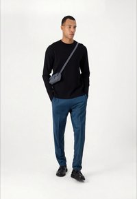 Black long-sleeve sweater paired with blue trousers. A small gray crossbody bag adds detail. Black shoes complete the outfit.