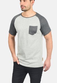 Light gray t-shirt with dark gray raglan sleeves and a chest pocket, made of soft cotton material; features a straight hem and tag at the bottom.