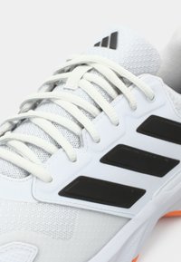 Λευκό αθλητικό παπούτσι με άνω μέρος από δίχτυ, μαύρες λεπτομέρειες στο πλάι και καμπυλωτή σόλα με πορτοκαλί διακοσμητικά στοιχεία. Οι κορδόνια είναι ανοιχτό γκρι.