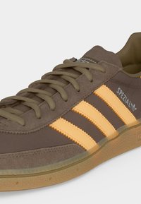 Καφέ sneaker Adidas Spezial με μπεζ ρίγες, επάνω μέρος από σουέτ και δέρμα και σόλα από καουτσούκ.