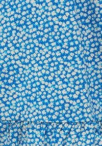 Tissu bleu présentant un délicat motif floral blanc, complété par une texture froncée le long de la couture inférieure.