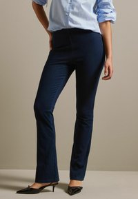 Navyblauwe fitted broeken met een gladde textuur, lichte flare bij de zoom en een hoge tailleband, gecombineerd met zwarte puntige hakken.