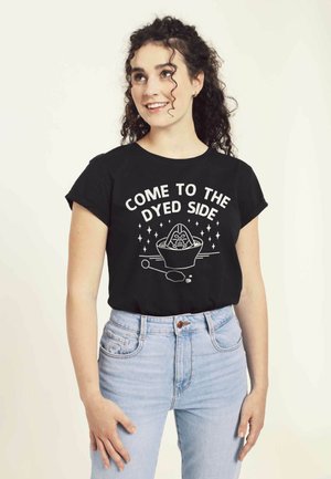 Sort bomulds T-shirt med korte ærmer, der har hvid tekst og grafisk design. Bæres med lyseblå højtaljede jeans.