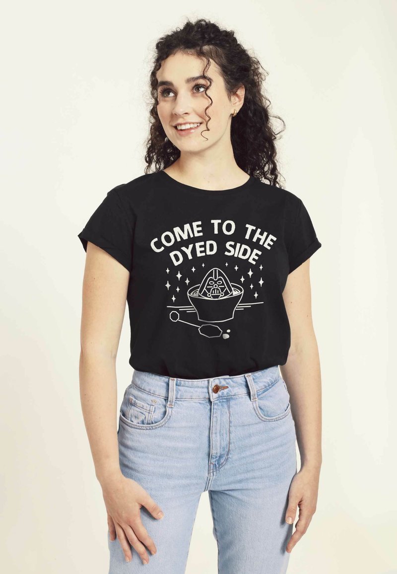 Camiseta de algodón negra con mangas cortas que presenta texto en blanco y un diseño gráfico. Se lleva con jeans de cintura alta de color azul claro.