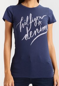 Mörkblå bomull t-shirt med grafiskt tryck i vitt med texten "hilfiger denim", korta ärmar och en figurnära design.