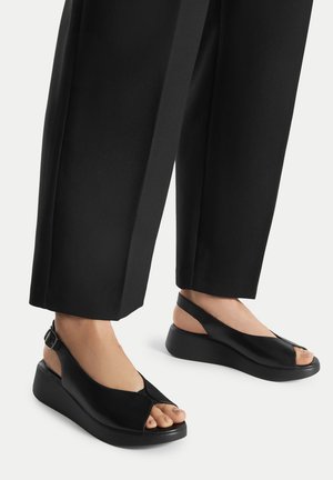 Sandali zeppa neri con design open-toe, realizzati in pelle liscia. Cinturino alla caviglia regolabile con tomaia testurizzata e suola nera solida.