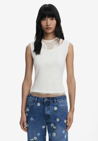 Witte geribbelde tanktop met kanten details bij de halslijn, gecombineerd met blauwe denim jeans met geborduurde madeliefjes.