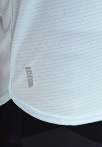 Jasnoniebieska koszulka sportowa z cienkimi poziomymi paskami, z metką logo na boku. Materiał wydaje się gładki i odprowadzający wilgoć.