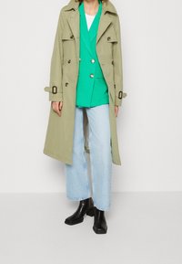 Khaki trenčkot, zelený blazer, bílý tričko, světle modré volné džíny a černé kotníkové boty. Kabát má knoflíky a pásky.