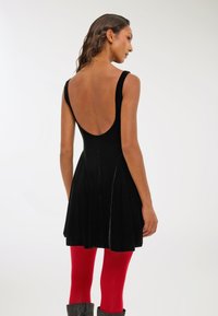 Czarna aksamitna sukienka bez rękawów z niskim dekoltem, rozkloszowanym dołem, w połączeniu z czerwonymi rajstopami i szarymi botkami. Gładka faktura, prosty design.