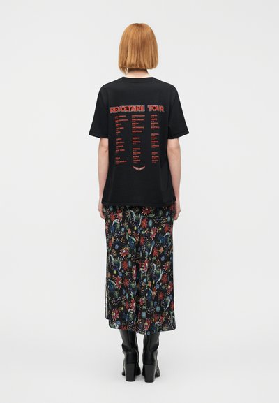 Μαύρο μπλουζάκι με το κείμενο "REVOLTAIRE TOUR" και τα ονόματα πόλεων σε κόκκινο στο πίσω μέρος, σε συνδυασμό με μακριά φούστα με λουλουδάτο σχέδιο και μαύρες μπότες.