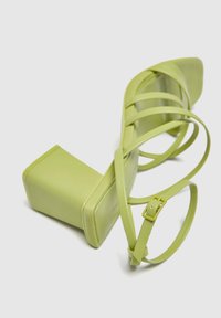 Sandal con tacco alto verde chiaro, a punta quadrata, tacco a blocco e numerose cinghie sottili, inclusa una cinghia con fibbia alla caviglia, su sfondo bianco.