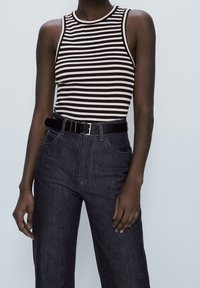 Black and white striped ribbed tank top with a crew neckline, paired with high-waisted dark denim jeans and a black belt.