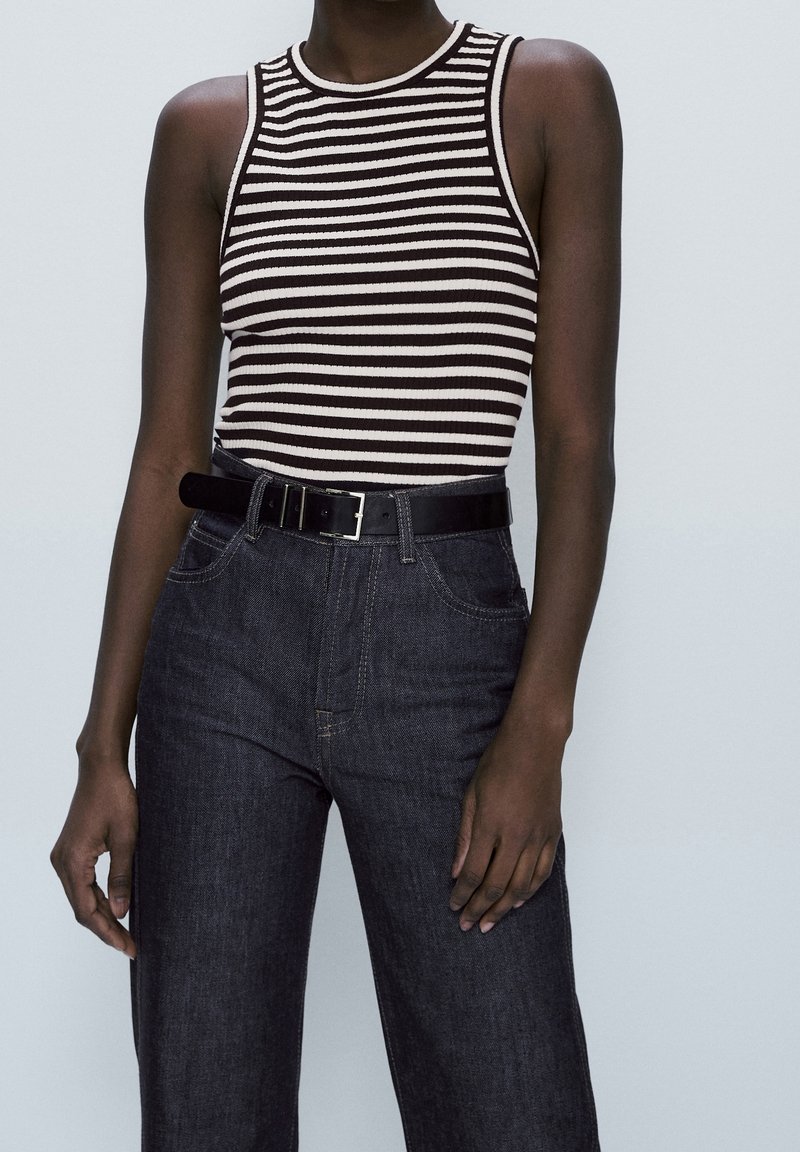Black and white striped ribbed tank top with a crew neckline, paired with high-waisted dark denim jeans and a black belt.