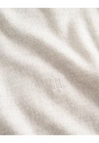 Weicher beige gestrickter Stoff mit einer subtil geprägten römischen Zahl II, die zentral auf dem Material platziert ist.