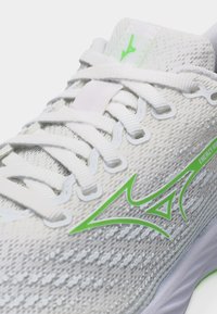 White running shoe with green logo, white laces, and textured fabric upper showcasing lightweight design details.