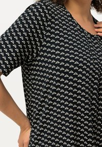 Schwarzes kurzärmliges Oberteil mit einem weißen Blumenmuster, runder Ausschnitt und flexiblem Baumwollmaterial. Das Design zeigt eine lässige Passform mit subtiler Textur.