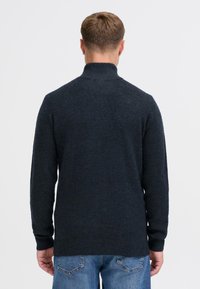 Donkergrijze gebreide trui met een hoge kraag, lange mouwen en een textuurafwerking. De achterkant toont een relaxte pasvorm en een eenvoudig ontwerp.