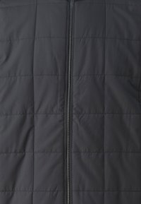 Colete acolchoado preto com textura matelassada, fecho frontal total e material leve. Ideal para sobreposições em clima mais fresco.