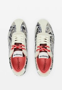 Texturierte Sneakers mit einem Schlangenledermuster in Schwarz und Weiß, cremigen Akzenten, roten Schnürsenkeln und rosa Innensohlen. Markenlogo auf der Zunge sichtbar.