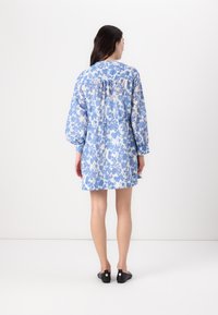 Rochie cu imprimeu floral albastru, cu mâneci lungi și spate ușor plisat. Material ușor, până la genunchi, asociată cu pantofi negri cu talpă joasă.