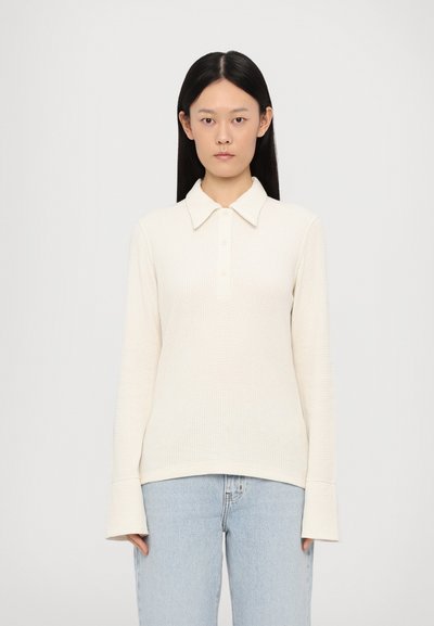 Long-sleeve, collared pullover in off-white waffle knit. Features a button placket and wide cuffs. Casual fit complements light blue jeans.