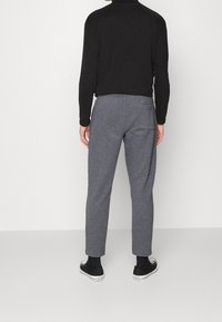 Graue Lounge-Hose mit lockerer Passform, aus weichem Stoff. Verfügt über eine Gesäßtasche und wird mit schwarzen High-Top-Sneakers getragen.