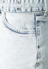 Világoskék farmernadrág, halovány mosással, fém kiegészítőkkel és előre elhelyezett zsebbel, finom varrási részletekkel.