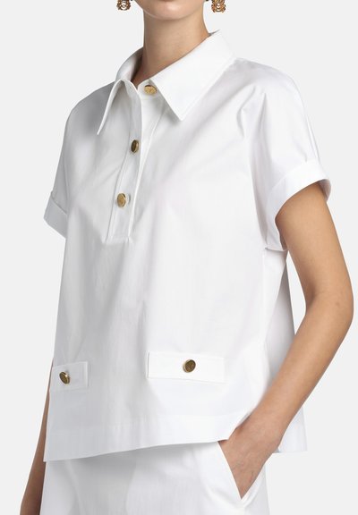 Fehér rövid ujjú ing galléros nyakkivágással, három arany gombbal, két gombbal zárható zsebbel és laza szabással.