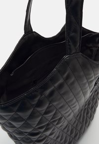 Quiltad svart tygväska i slät material, med två stadiga handtag och en innerficka med dragkedja för säker förvaring.