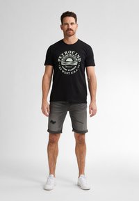 Zwart katoenen T-shirt met een grafisch ontwerp aan de voorkant, met een zonsopgang, in combinatie met grijze denim shorts met versleten accenten en omgeslagen pijpen.