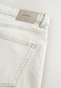 Bijele traperice od denima s ušivenim džepom, suptilnom teksturom i smeškom kožnom oznakom s natpisom "DENIM SUPPLY" na struku.