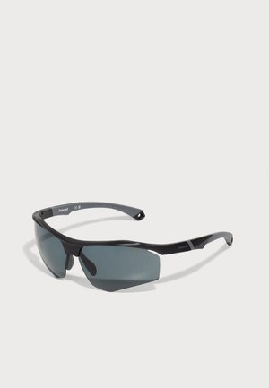 Melnas sporta saulesbrilles ar pelēkiem polarizētiem stikliem, elegants dizains, apjozoša forma un teksturēti mīkstie iemaukti.