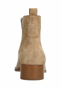 Bottine en daim beige avec côtés texturés, languette de tirage cousue à l'arrière, talon bloc en bois et fermeture éclair latérale visible de l'arrière.