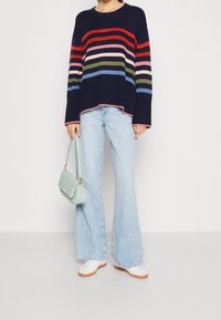 Marinrandig tröja i olika färger, parat med ljusblå utsvängda jeans. Accessoarer med en mintgrön handväska och vita skor.