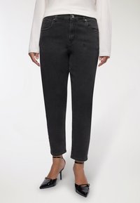 Czarne dżinsy o prostym kroju, pięć kieszeni, widoczne szwy; noszone z lakierowanymi czarnymi szpilkami.