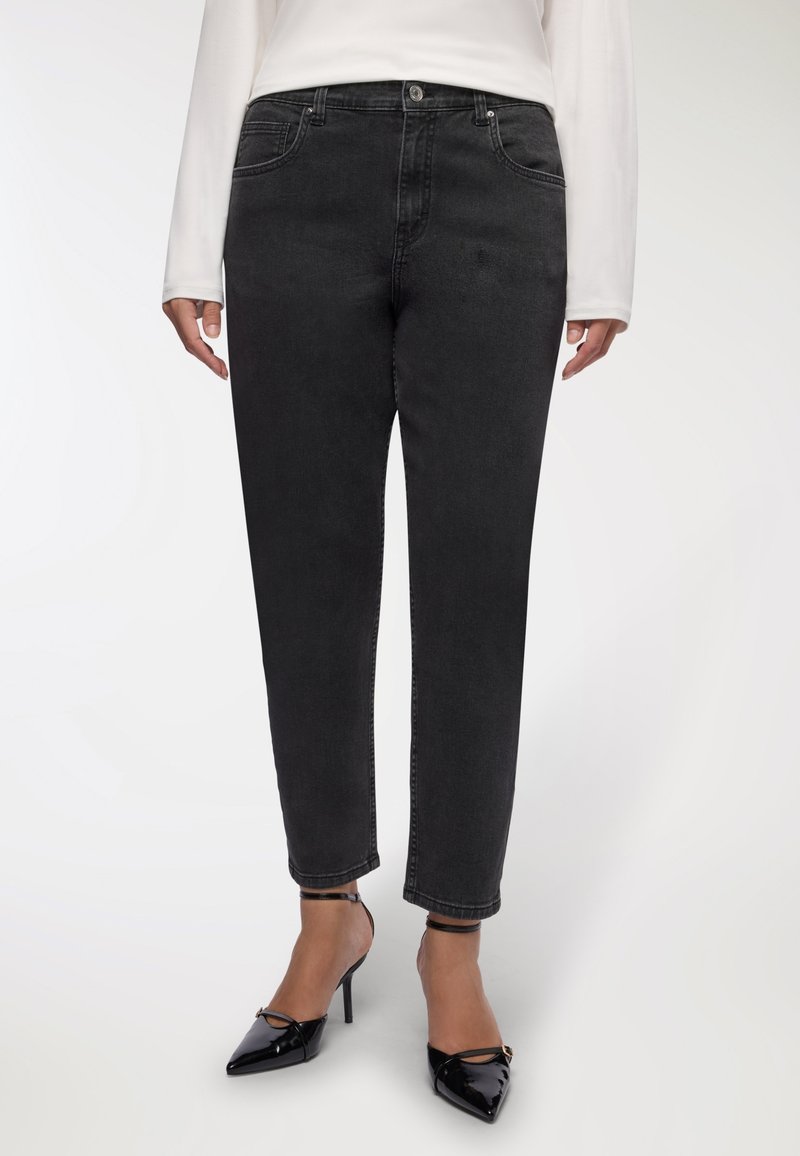 Czarne dżinsy o prostym kroju, pięć kieszeni, widoczne szwy; noszone z lakierowanymi czarnymi szpilkami.