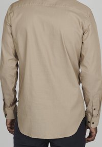 Button-up skjorta i beige tyg med en texturerad mönster, med långa ärmar, rundad nederkant och knappmanschetter.