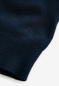 Mornarsko modra pletena jopica z rebrastim robom in manšetami, s subtilnim vezenim logotipom v usklajeni barvi. Mehak, teksturiran material.