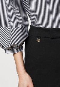 Svart blyertskjol med guldfärgad detalj, kombinerad med en blus i svart och vitt med puffärmar och manchesterfåll.