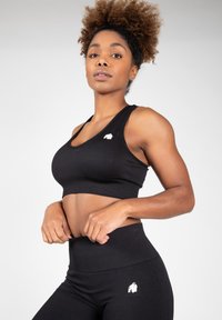 Černý sportovní crop top a legíny s vysokým pasem, obojí vyrobené z hladké, elastické tkaniny; na levé straně se nachází malé bílé logo.