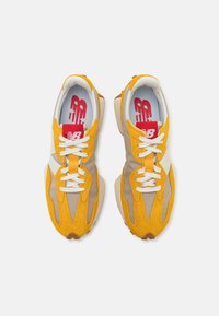 Sneakers with a mix of yellow suede and tan fabric. White laces and accents. Red logo tag visible inside. Rounded rubber outsole.